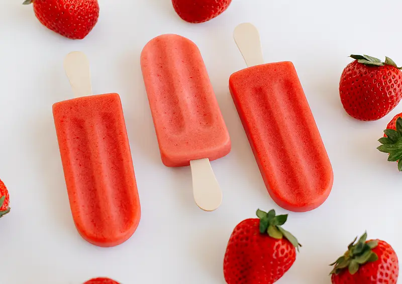 3 strawberry popsicles surrounded by strawberries